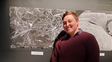School of Biology and Ecology student Sadia Crosby stands to the right of a large print. The print is a highly-magnified image of browntail moth hairs.
